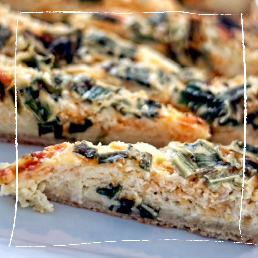 Goldbraune Wildkräuter-Quiche mit Wegwarte, grünem Lauch und gereiftem Ziegenkäse auf rustikalem Holztisch