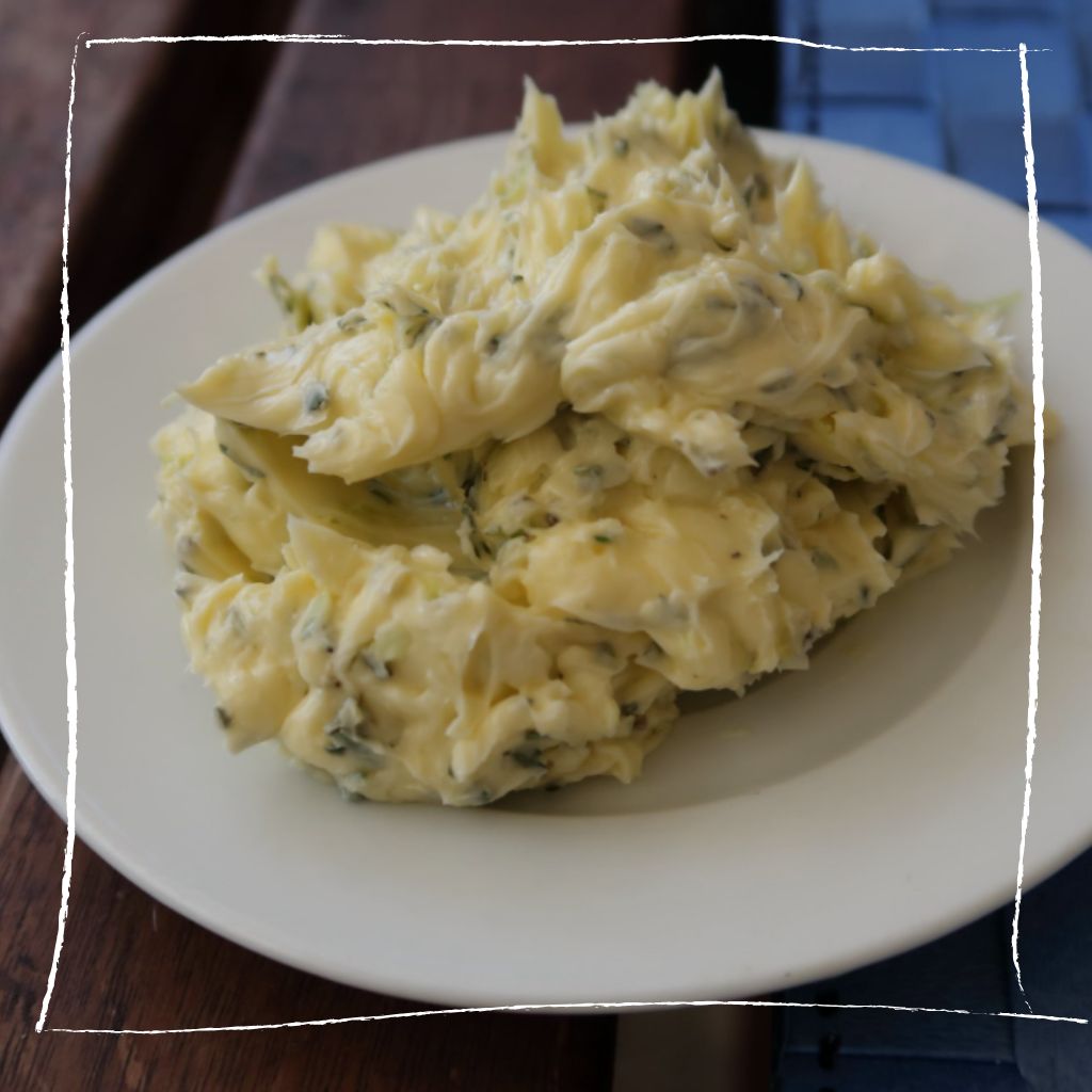 Elegante Spitzwegerich-Kräuterbutter mit Zitronensalz auf Holzbrett angerichtet