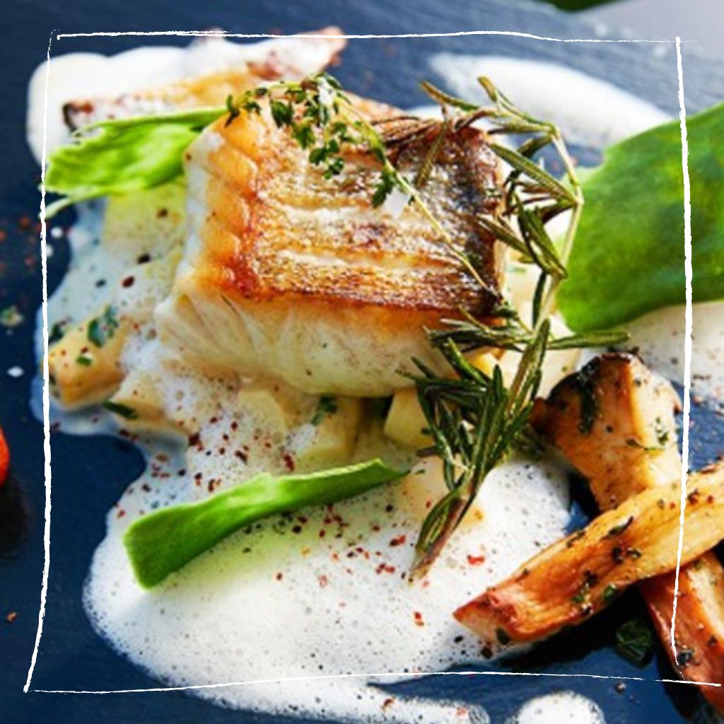 Elegantes Zanderfilet auf cremigem Ehrenpreis-Buttermilch-Schaum mit grünem Erbsenpüree und blauer Blütendekoration auf weißem Teller